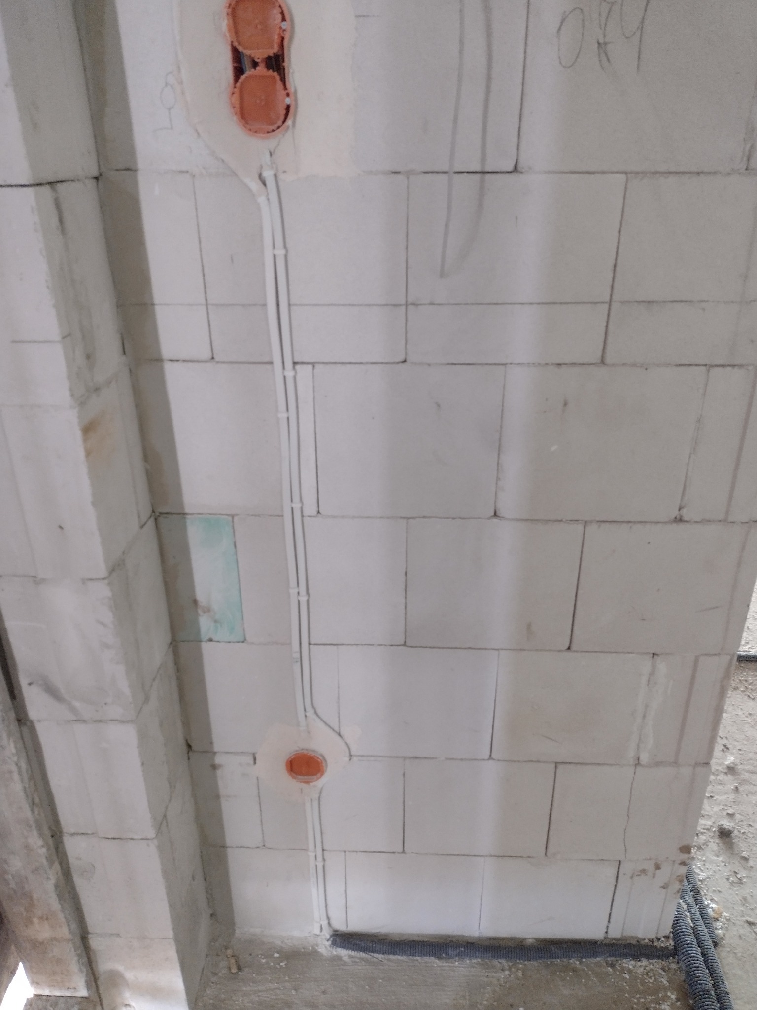 Wewnętrzna instalacja elektryczna w surowym budynku z bloczków, widoczne puszki podtynkowe i przewody prowadzone po ścianie, fragment podłogi z rurami karbowanymi.