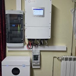 PV-EL - Biały inwerter Solis, obok rozdzielnica i magazyn energii Kon-TEC na kółkach, zamontowane na beżowej ścianie w pomieszczeniu. Widoczne okablowanie i licznik.