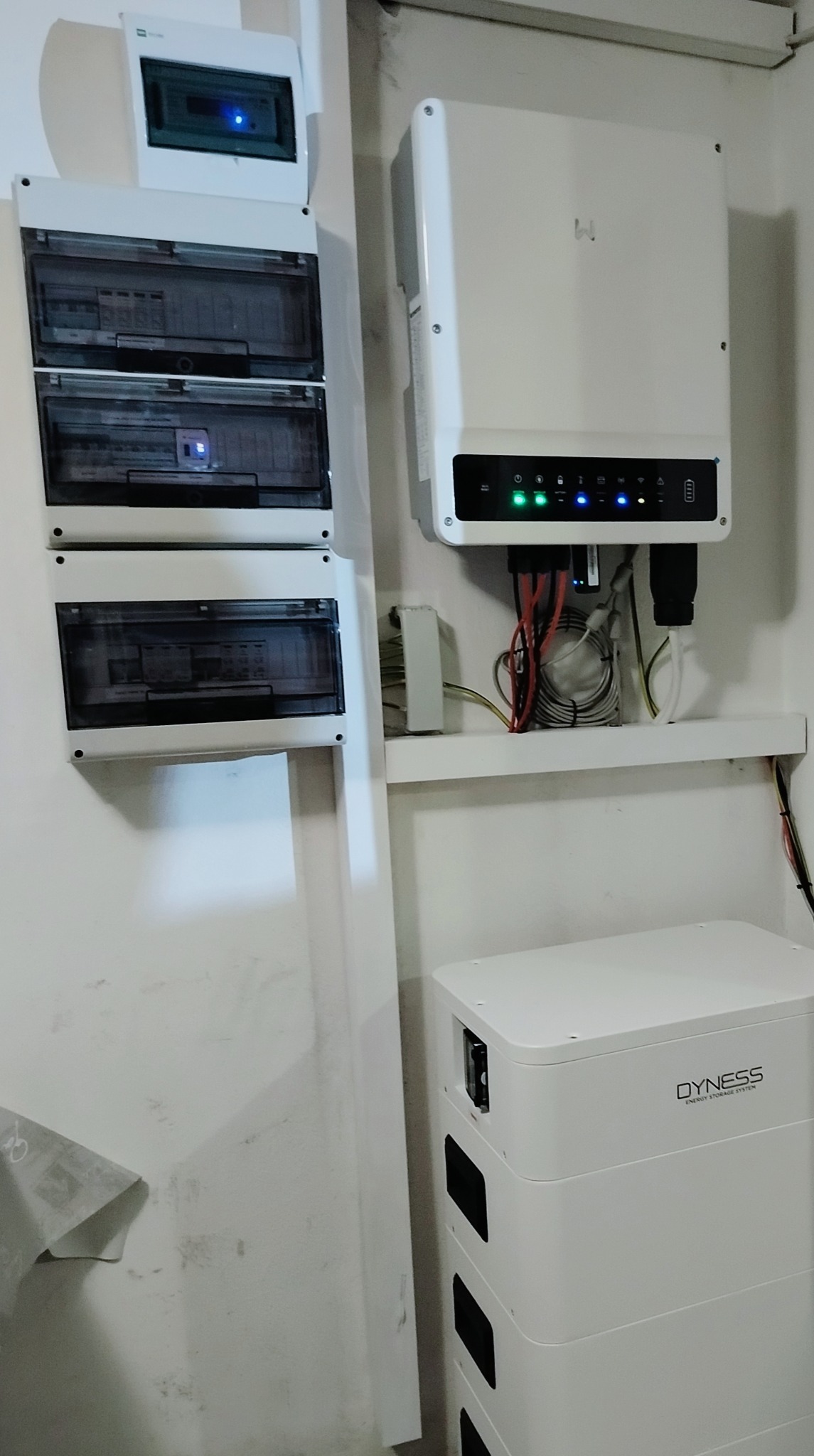 Biała instalacja z inwerterem, baterią magazynu energii Dyness i rozdzielnicą elektryczną na ścianie.