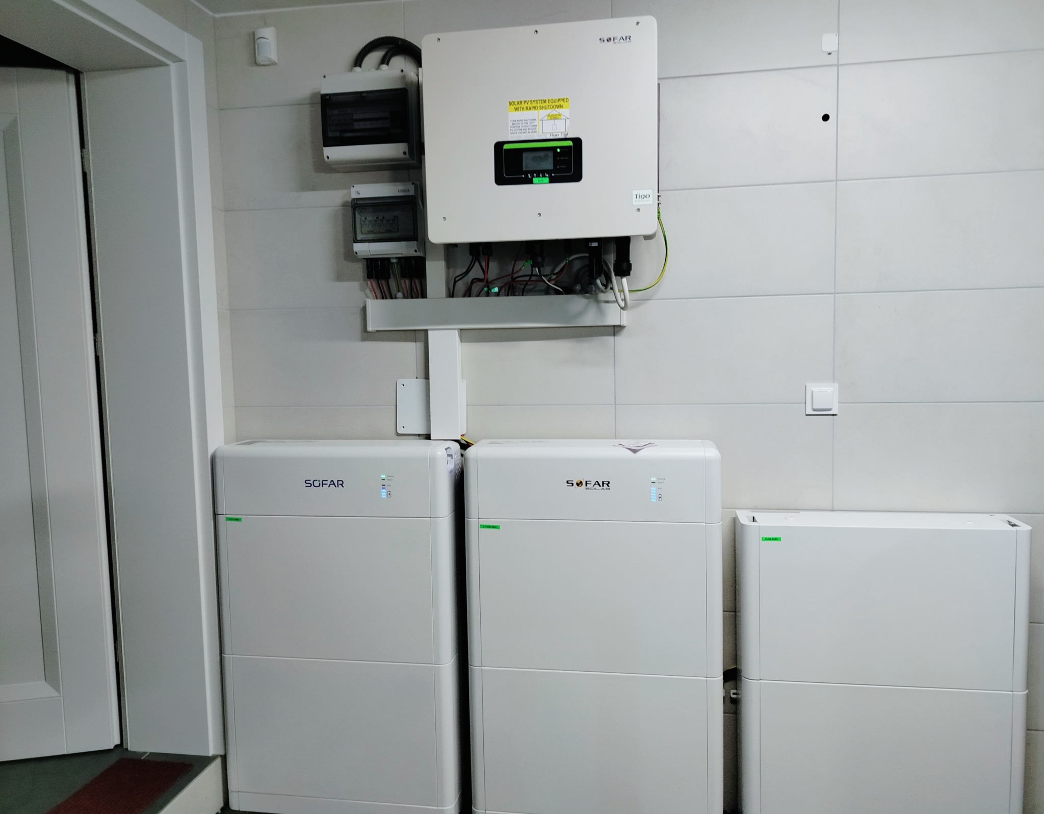 Białe moduły magazynu energii Sofar, falownik i skrzynki zabezpieczeń zamontowane na białej ścianie w pomieszczeniu technicznym, widoczne przewody.
