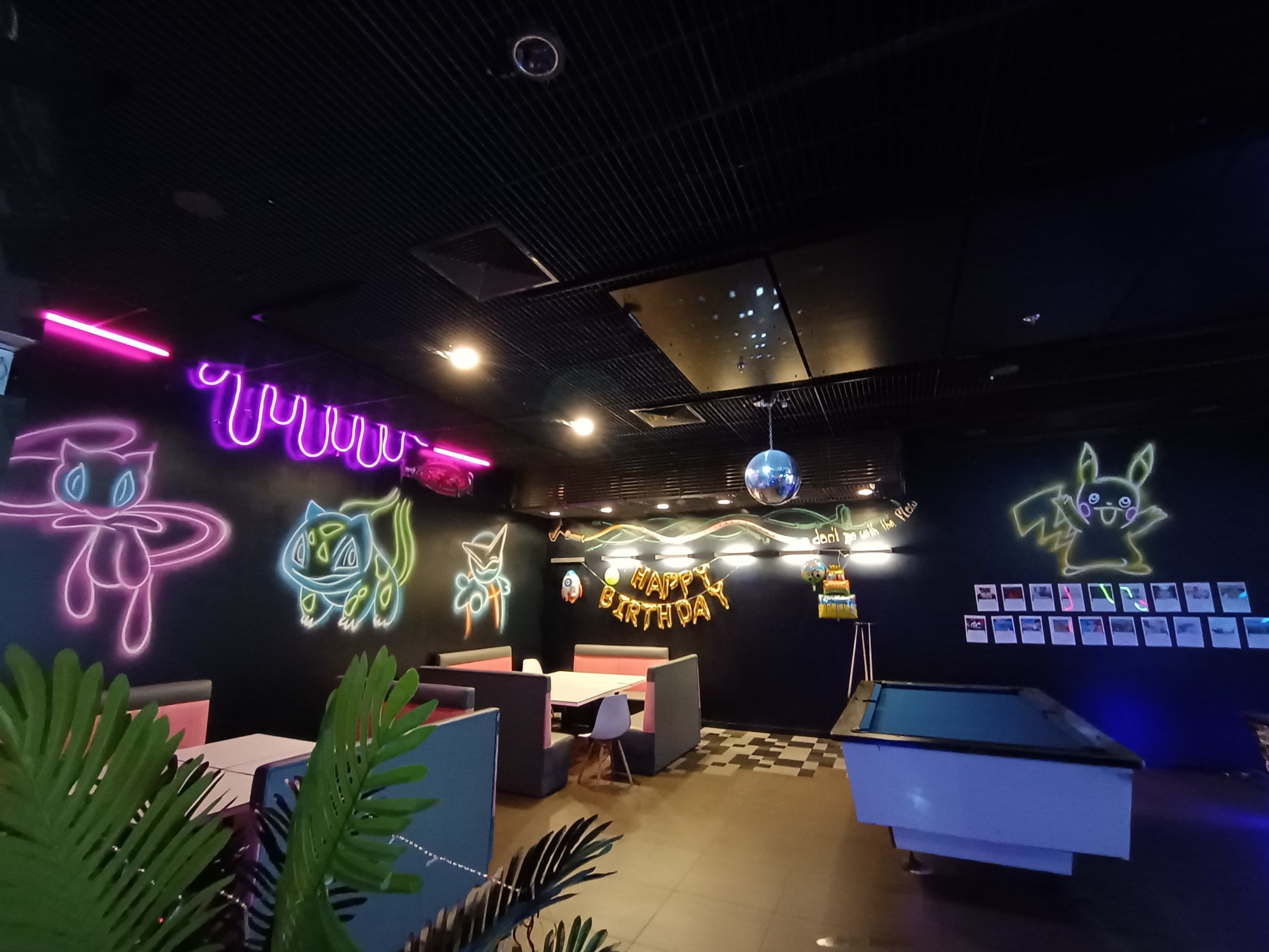Salon gier z neonowymi dekoracjami Pokemon, stołem bilardowym i girlandą urodzinową.