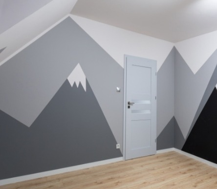 Pokój w odcieniach szarości z motywem gór na ścianach, jasne panele podłogowe i szare drzwi.