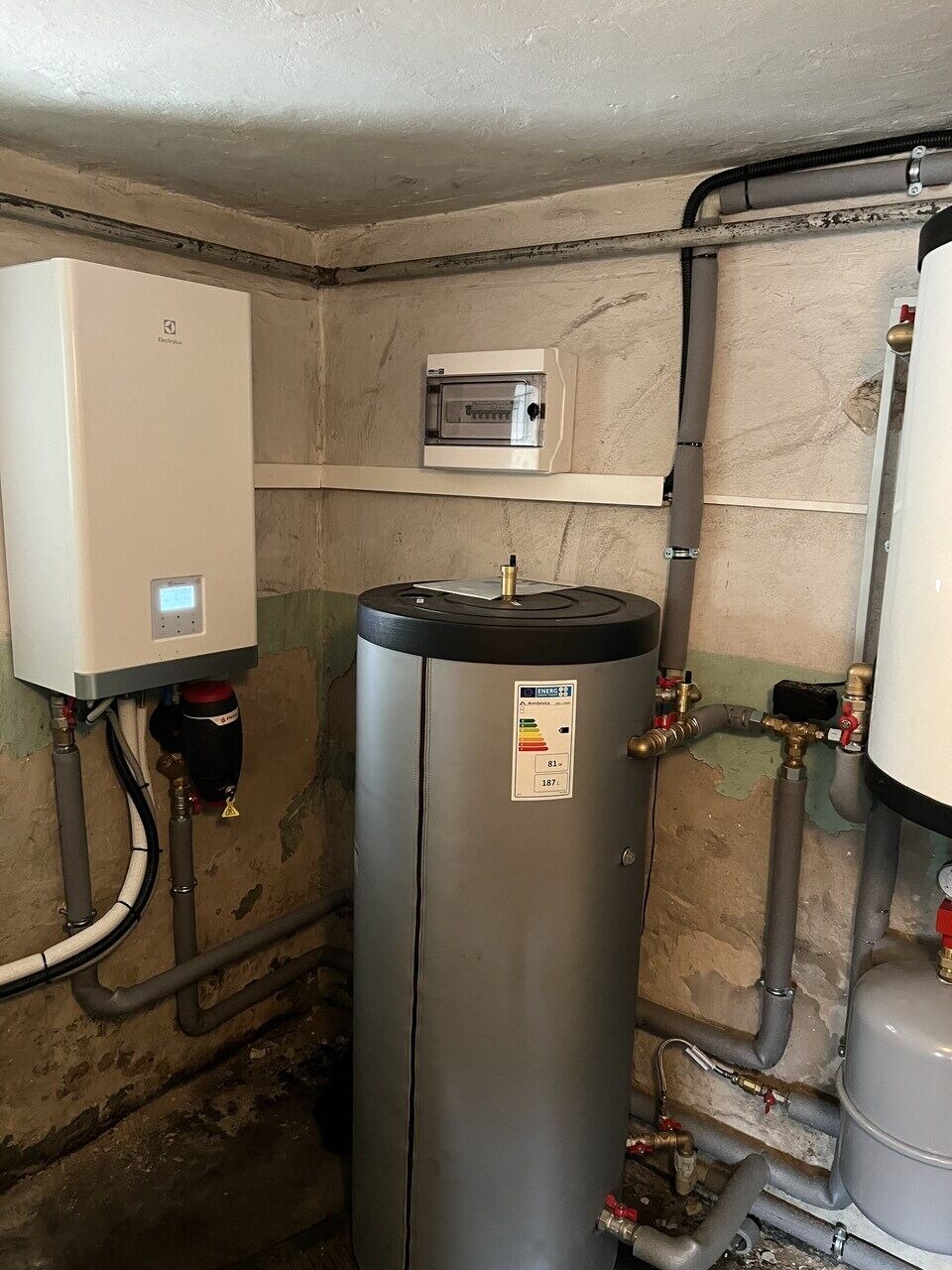 Instalacja pompy ciepła Electrolux z zasobnikiem ciepłej wody w piwnicy, widoczna skrzynka elektryczna i rury.