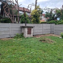 Ogrody Bonsai Damian Kopiec - Szary płot betonowy z geometrycznym wzorem, otaczający trawnik z murowanym grillem i stertą gałęzi. W tle domy i wysokie drzewa.
