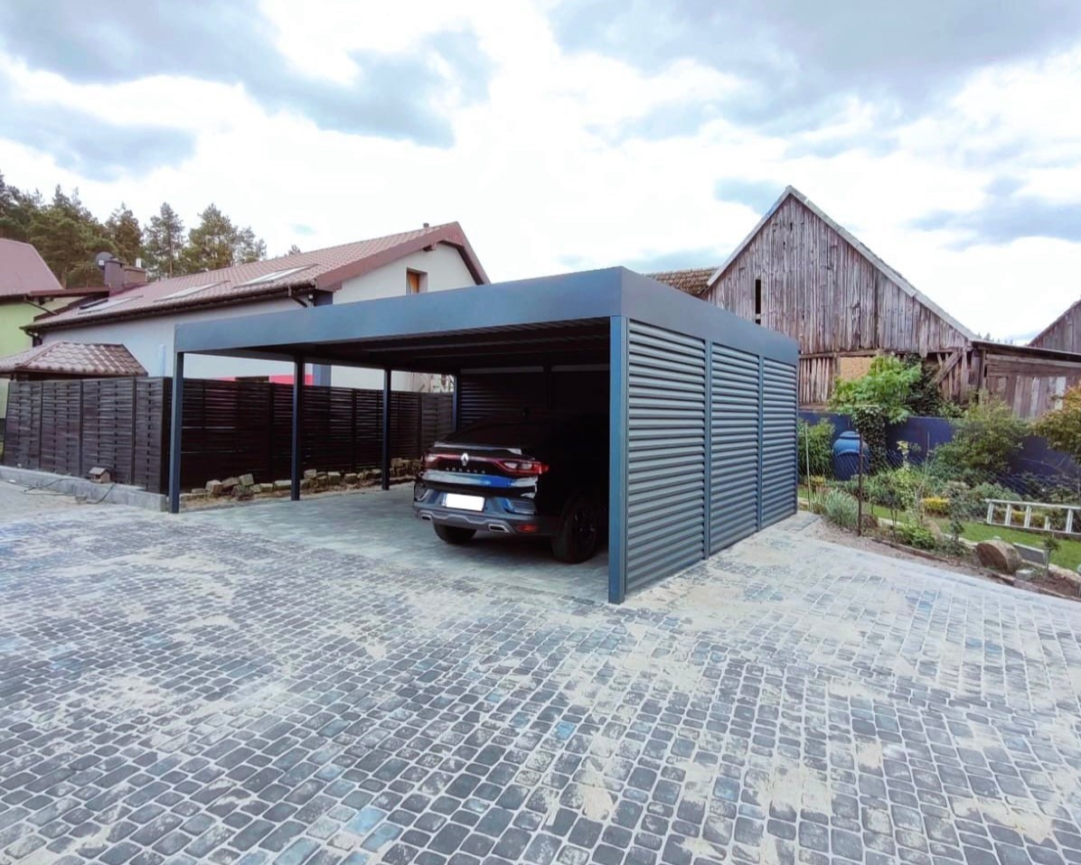 Nowoczesna, szara pergola metalowa z lamelami, chroniąca zaparkowany samochód na posesji z kostki brukowej. W tle dom i drewniana stodoła.