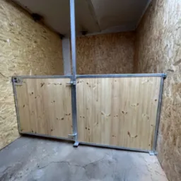 Wnętrze pomieszczenia wykończonego płytami OSB z niskim, drewnianym ogrodzeniem z metalowymi ramami, tworzącym boks.