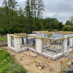 Sharim Invest Sp. Z o. o. - Stan surowy otwarty domu jednorodzinnego w Warszawie, widoczne ściany z betonu komórkowego i szalunki, teren wokół w stanie przygotowania pod dalsze prace.