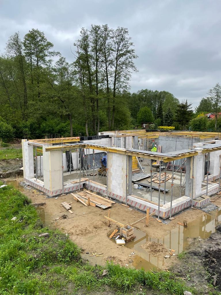 Stan surowy otwarty domu jednorodzinnego w Warszawie, widoczne ściany z betonu komórkowego i szalunki, teren wokół w stanie przygotowania pod dalsze prace.