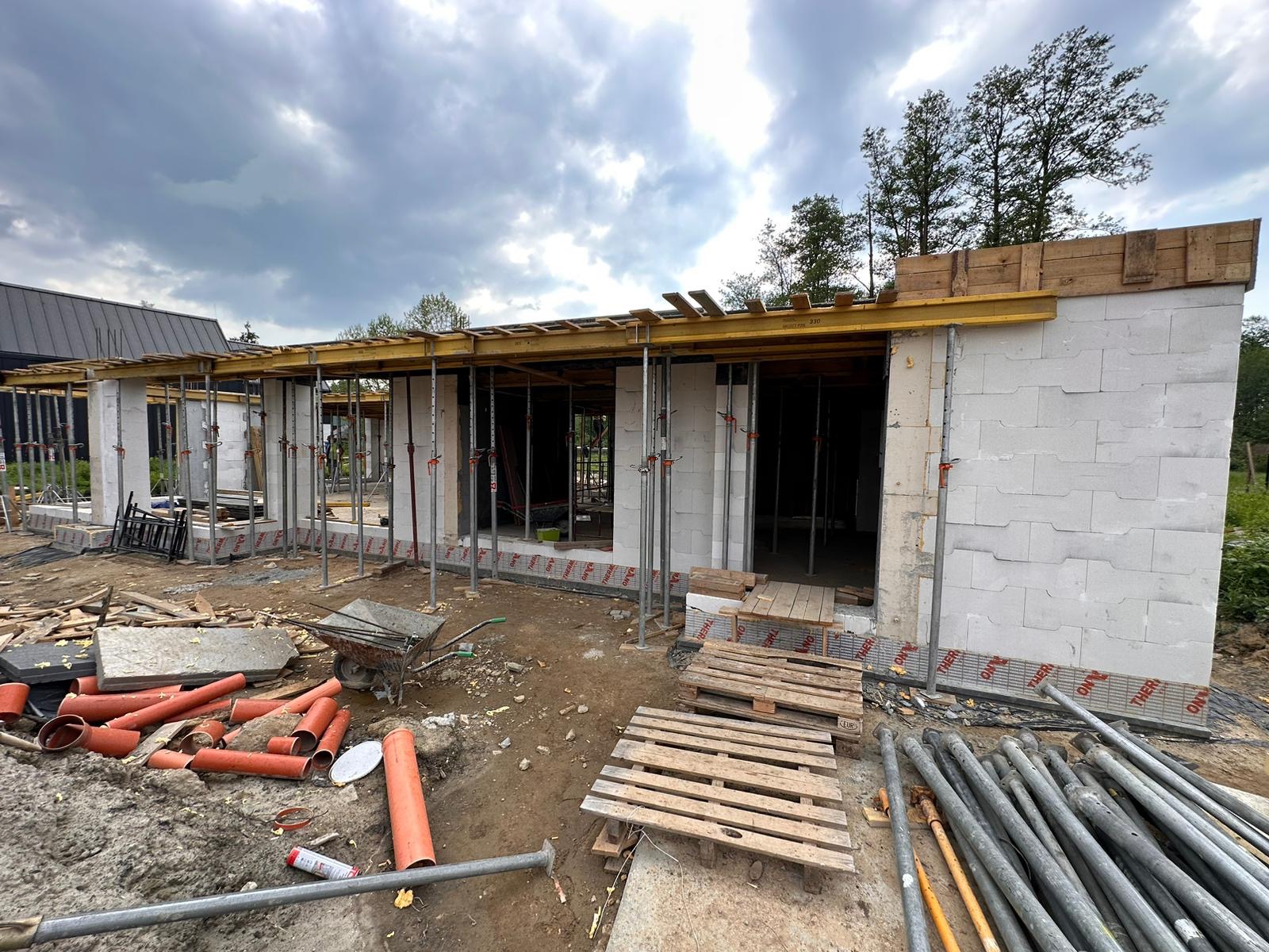 Budowa domu jednorodzinnego w stanie surowym otwartym: ściany z betonu komórkowego, podpory stropowe, widoczne materiały budowlane na placu budowy, pochmurne niebo.