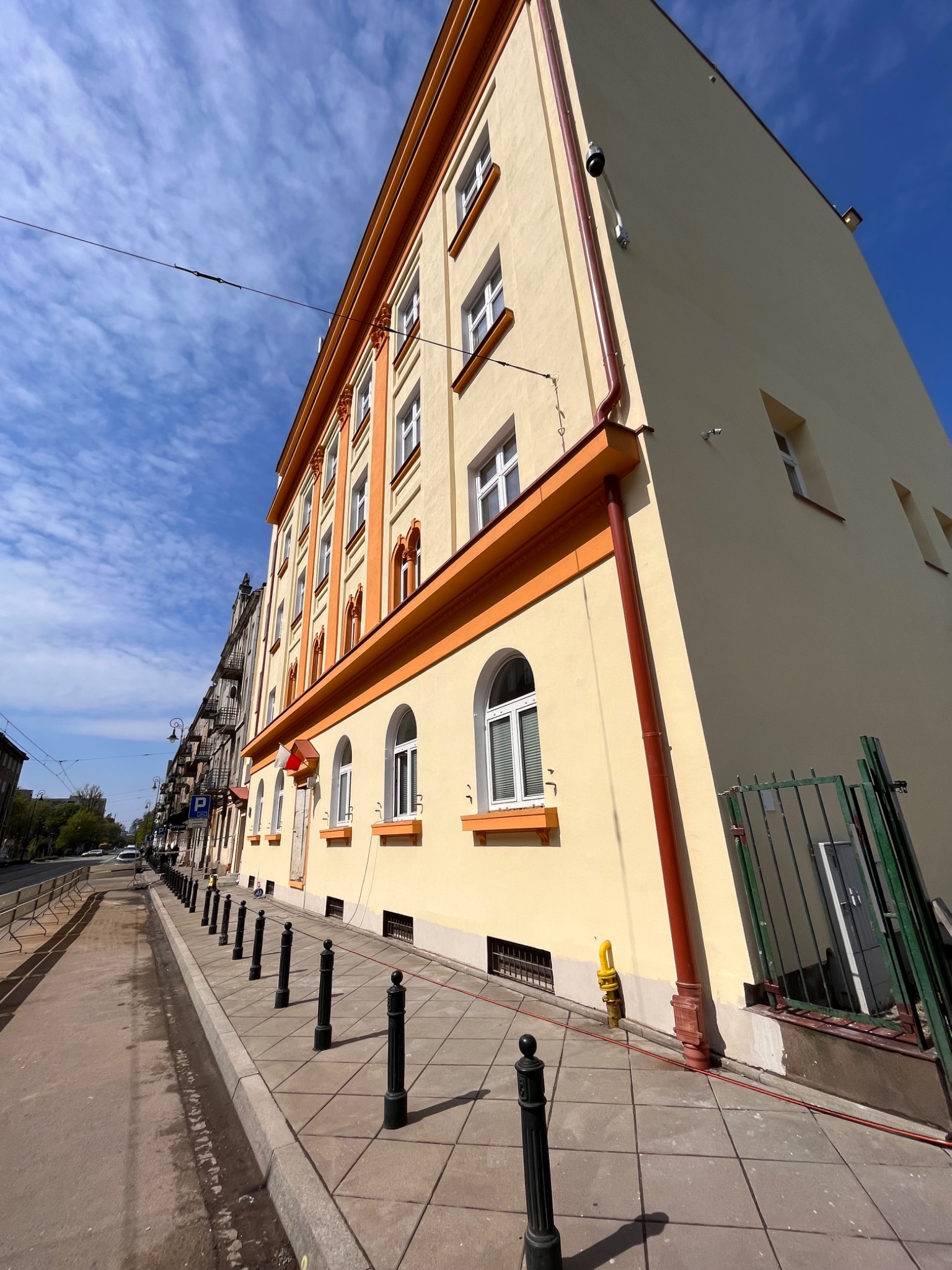 Odnowiona fasada budynku z beżową elewacją i pomarańczowymi detalami architektonicznymi, widok z poziomu chodnika w słoneczny dzień.