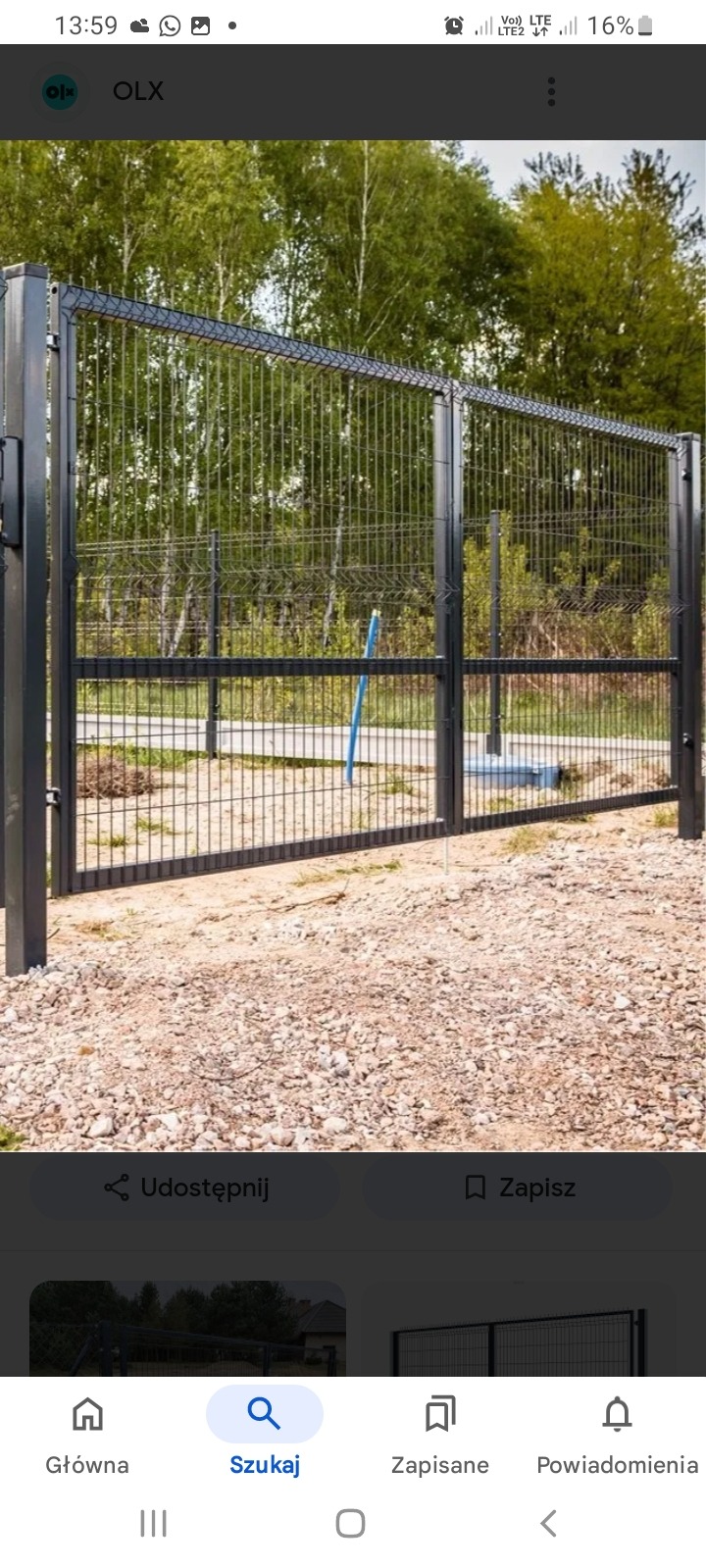 Nowoczesne, metalowe ogrodzenie panelowe w kolorze grafitowym, z widocznymi słupkami i siatką, na tle drzew i nieutwardzonego gruntu.