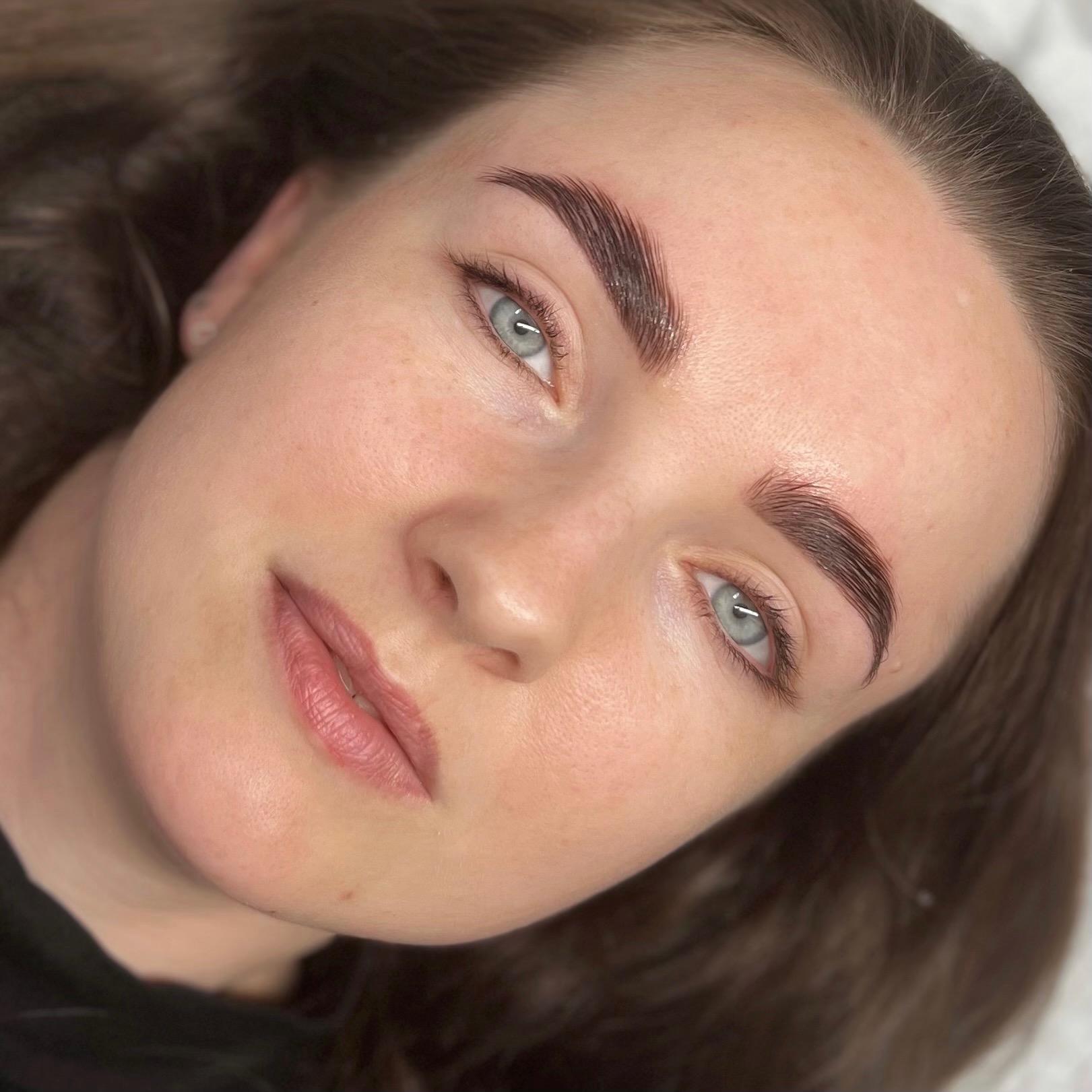 Zbliżenie na twarz kobiety z widocznymi brwiami po laminacji, z delikatnym błyskiem i precyzyjnym ułożeniem włosków, podkreślającym naturalny łuk brwiowy.