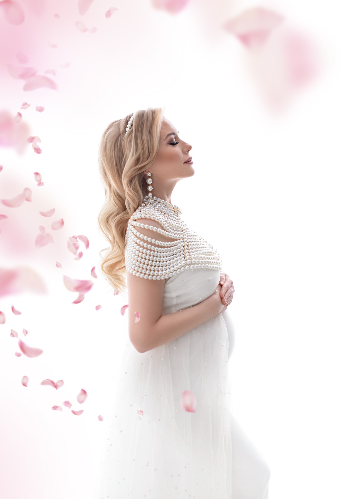 Portret profilowy kobiety w ciąży, ubranej w białą suknię i perłową biżuterię, otoczonej opadającymi płatkami róż na jasnym tle.