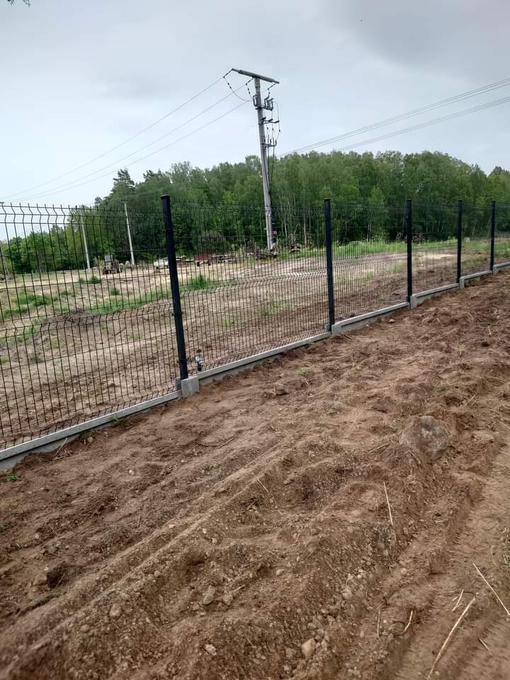 Nowo postawione, czarne ogrodzenie panelowe na betonowej podmurówce w Obiecanowie, z widoczną linią energetyczną w tle.