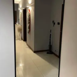 Prostokątne lustro w czarnej ramie zawieszone na ścianie w przedpokoju, odbijające wnętrze z lśniącą podłogą, dekoracjami świątecznymi i odkurzaczem pionowym.