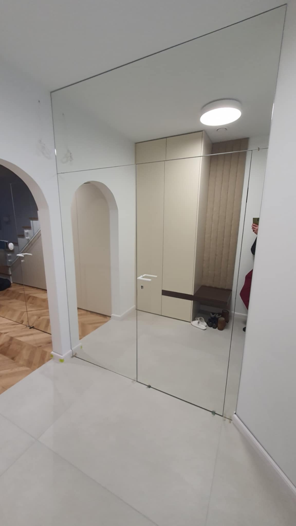 Szklana ściana działowa w przedpokoju, z widocznym wejściem łukowym i szafą wnękową. Minimalistyczny design, jasne kolory, odbicie w szkle.