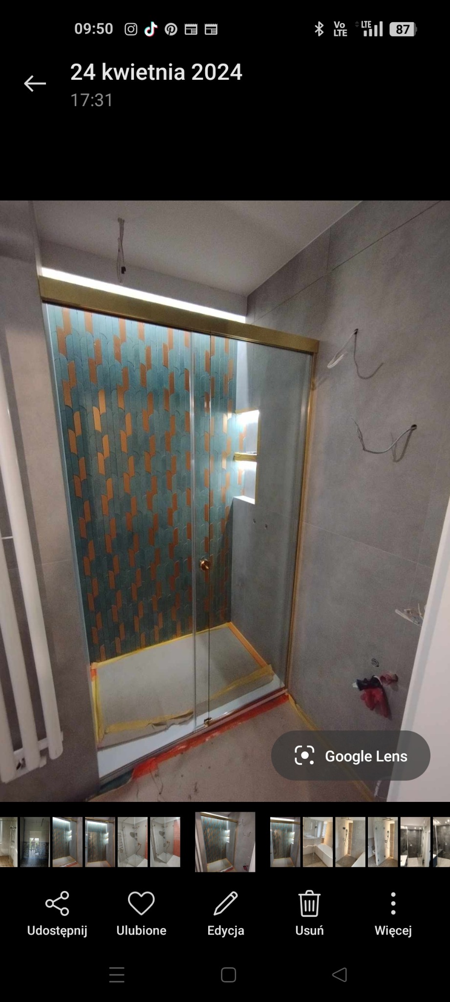 Kabina prysznicowa ze złotymi profilami i dekoracyjną ścianą z mozaiki w kształcie rybiej łuski. Widoczne niedokończone wykończenia podłogi.