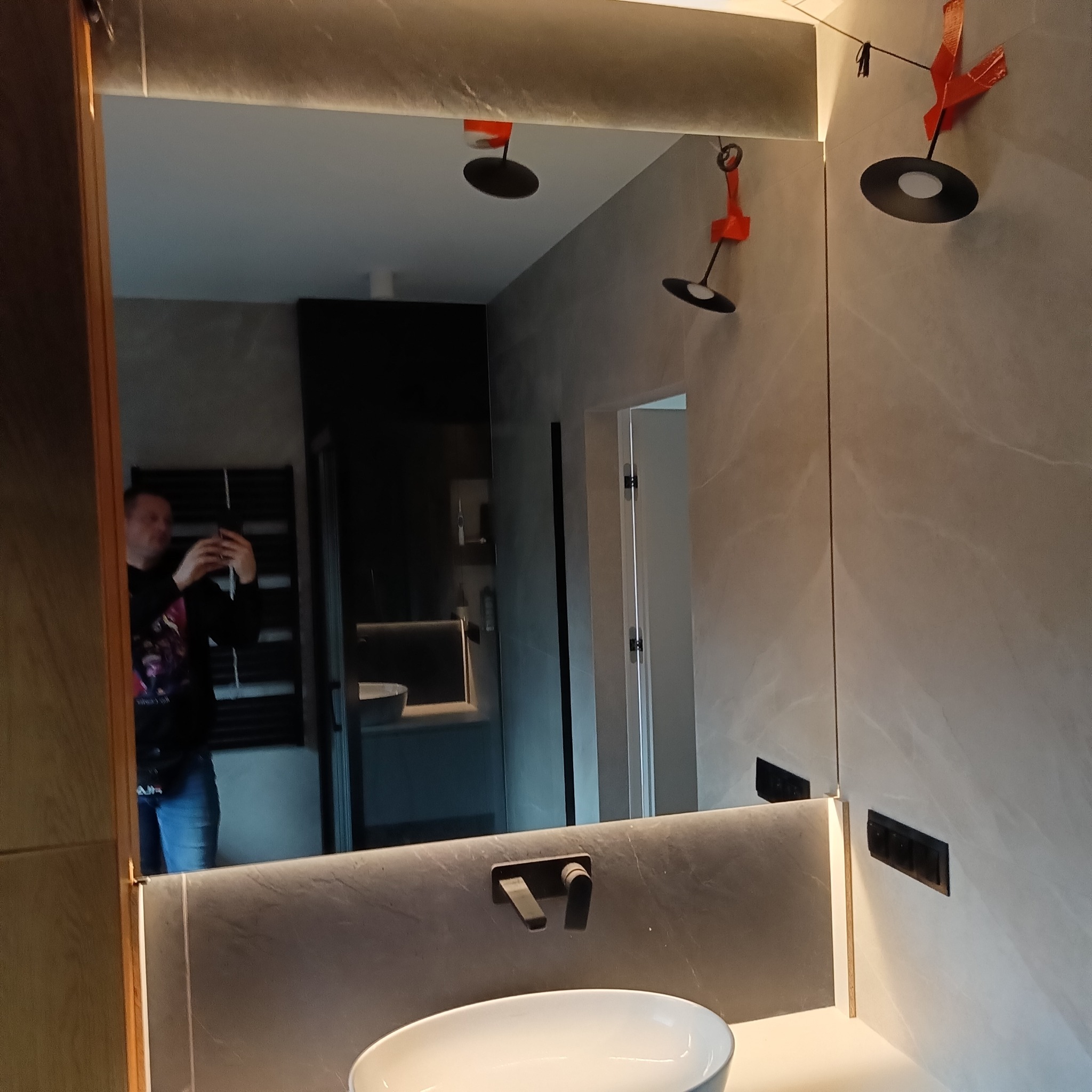 Nowoczesna łazienka w Warszawie z lustrem na wymiar i podświetleniem LED. Widoczne odbicie osoby robiącej zdjęcie. Minimalistyczny design i eleganckie wykończenie.