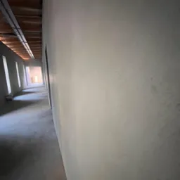 Korytarz w stanie surowym w Zaworach, ściany przygotowane pod malowanie, widoczne ślady szpachlowania i nier&oacute;wności na powierzchni.