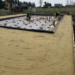 PEDRO-POLAKO Lucas VLASÁK - Przygotowanie zbrojenia fundamentów pod budowę domu. Widoczni pracownicy w odblaskowych kamizelkach i koparka w tle. Ujęcie z góry, ukazujące siatkę zbrojeniową.