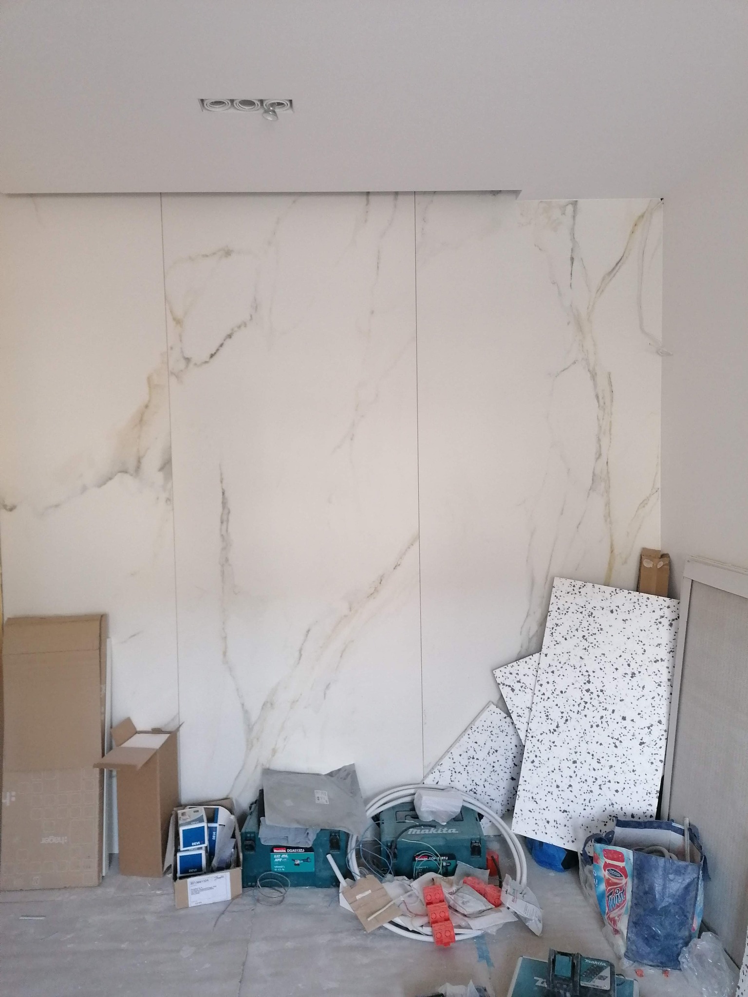Montaż wielkoformatowych płytek imitujących marmur na ścianie, widoczne narzędzia i materiały budowlane, surowy stan wykończenia.