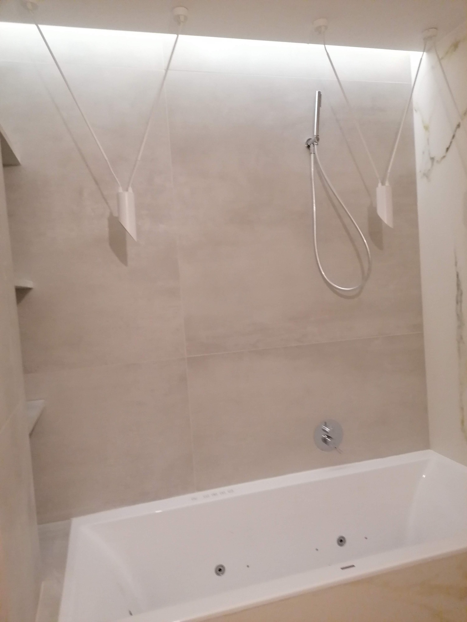 Nowoczesna łazienka z beżowymi płytkami, białą wanną z hydromasażem i oryginalnym oświetleniem sufitowym.