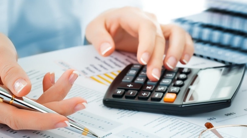 Dłonie kobiety z perfekcyjnym manicure, używającej kalkulatora nad arkuszem kalkulacyjnym, z piórem w dłoni, w jasnym biurze.