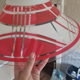 Asia Asia - Szklany, biało-czerwony klosz lampy z geometrycznym wzorem, trzymany w dłoni, widoczne zabrudzenia na kloszu i w tle.