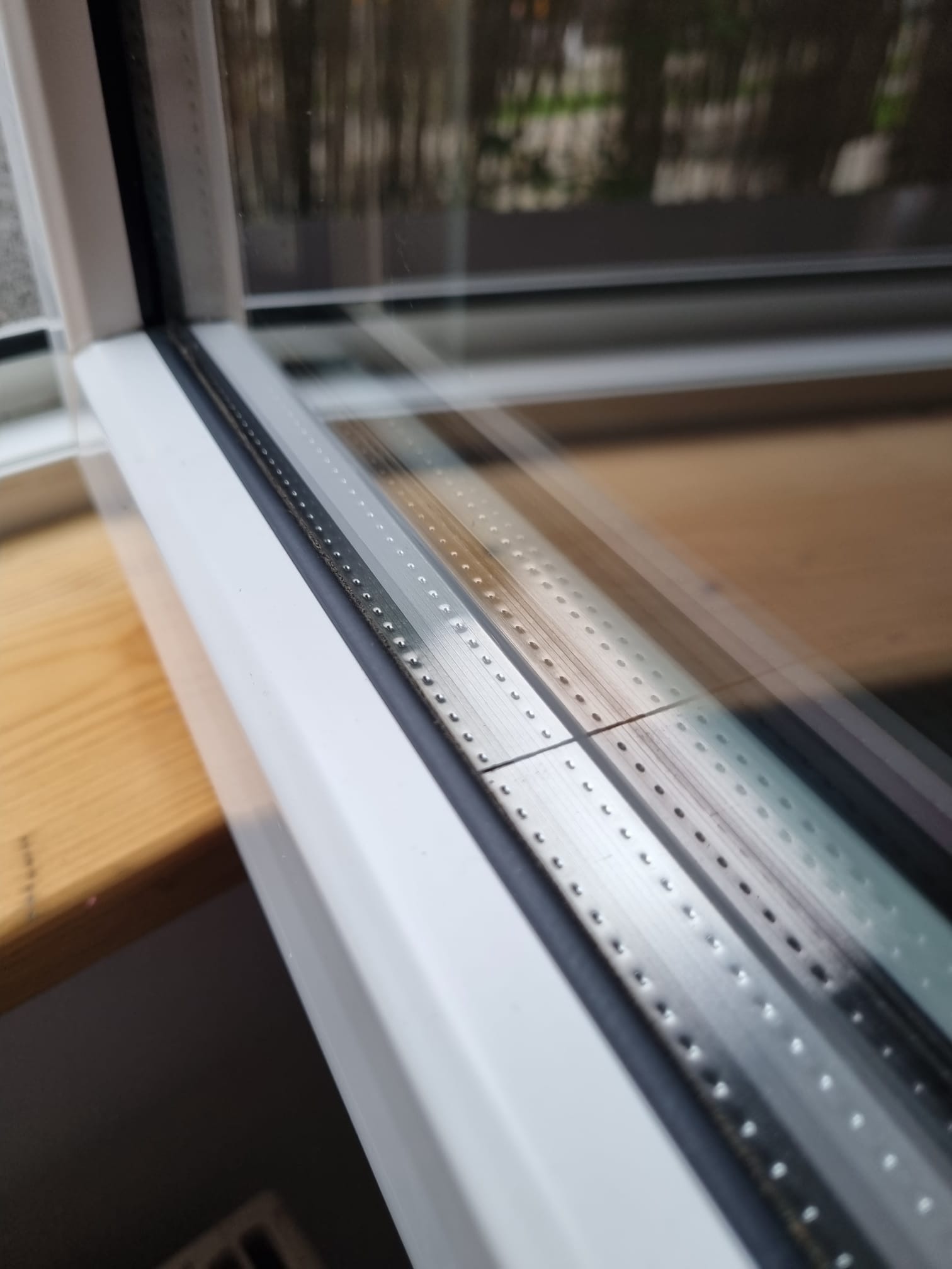 Szczegółowe ujęcie okna PCV z widoczną uszczelką i aluminiowymi elementami konstrukcyjnymi, odbijającymi światło dzienne.