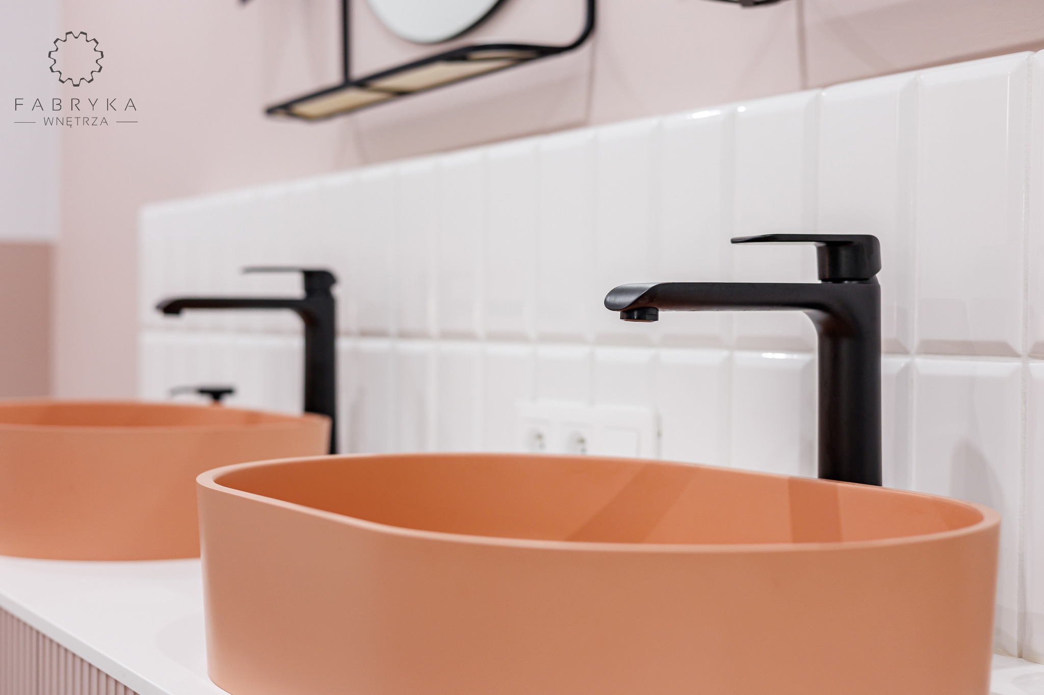 Dwie identyczne, łososiowe umywalki nablatowe z czarnymi, minimalistycznymi bateriami na białym blacie, białe kafelki na ścianie, logo firmy Fabryka Wnętrza w lewym górnym rogu.