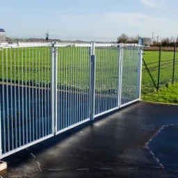 Automatyczna brama wjazdowa ze stali ocynkowanej, z napędem i przyciskami sterującymi, na tle zielonego krajobrazu.