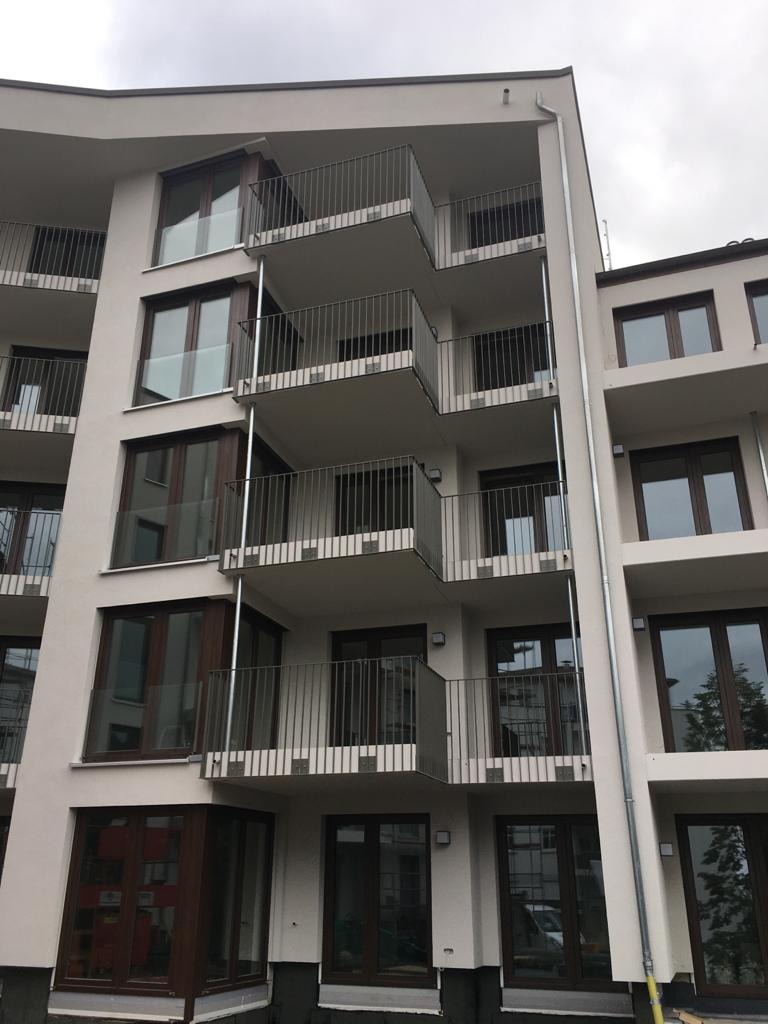 Nowoczesny budynek wielorodzinny z balkonami zabezpieczonymi metalowymi balustradami o minimalistycznym designie, widok z dołu na kilka pięter.