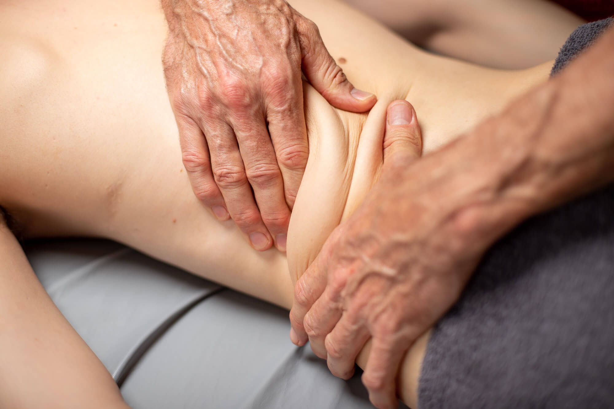 Dłonie terapeuty uciskają skórę na boku pacjenta podczas zabiegu. Widoczne zmarszczki na dłoniach masażysty.