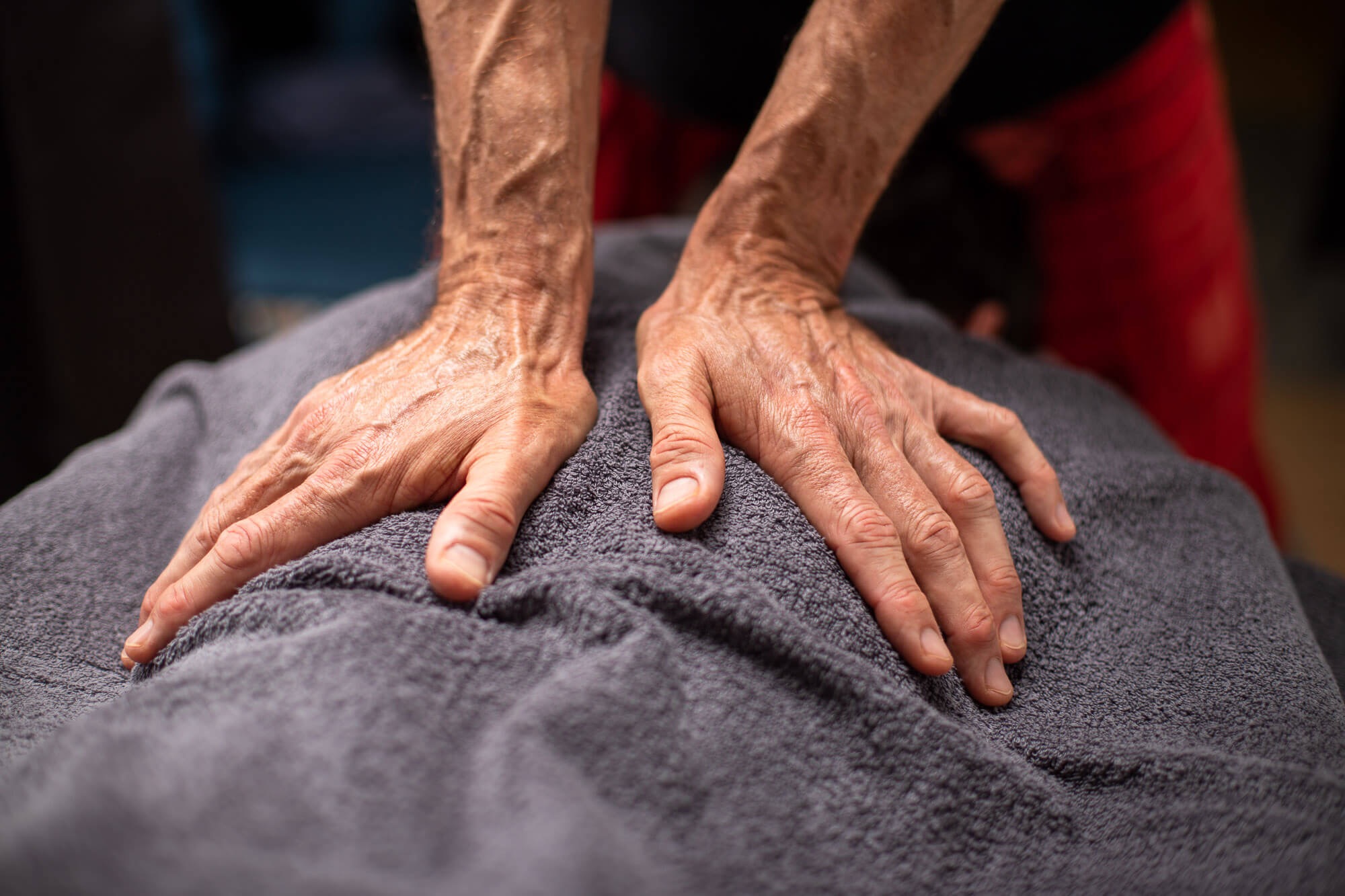 Dłonie terapeuty z wyraźnie widocznymi żyłami na plecach klienta przykrytych szarym ręcznikiem podczas sesji