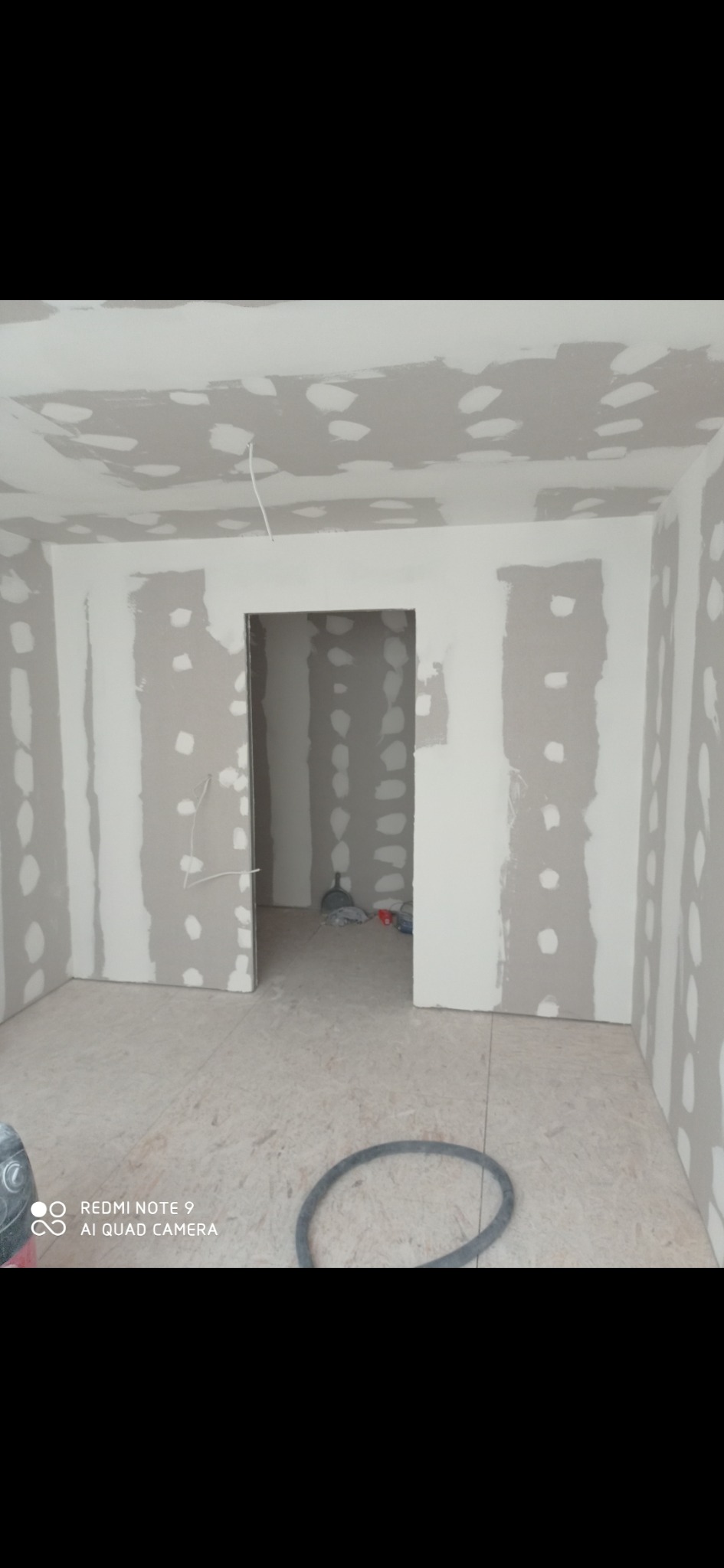 Surowe ściany z płyt gipsowo-kartonowych, wstępnie zagruntowane i przygotowane do dalszych prac wykończeniowych, widoczne narzędzia budowlane w tle.