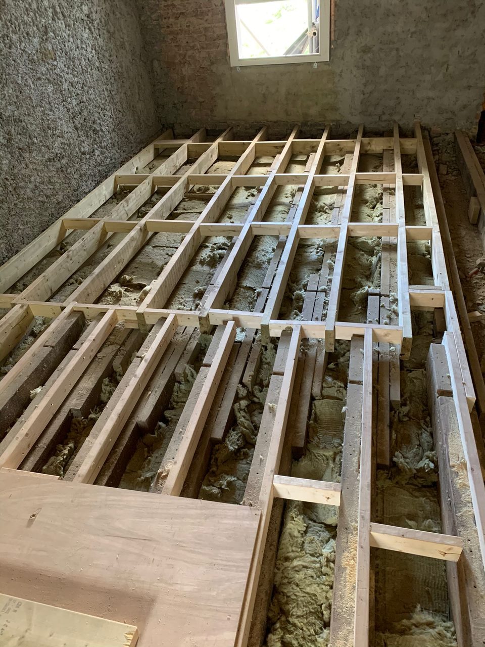 Drewniana konstrukcja pod podłogę z izolacją z wełny mineralnej, widok z dołu na okno dachowe, surowe wykończenie ścian.