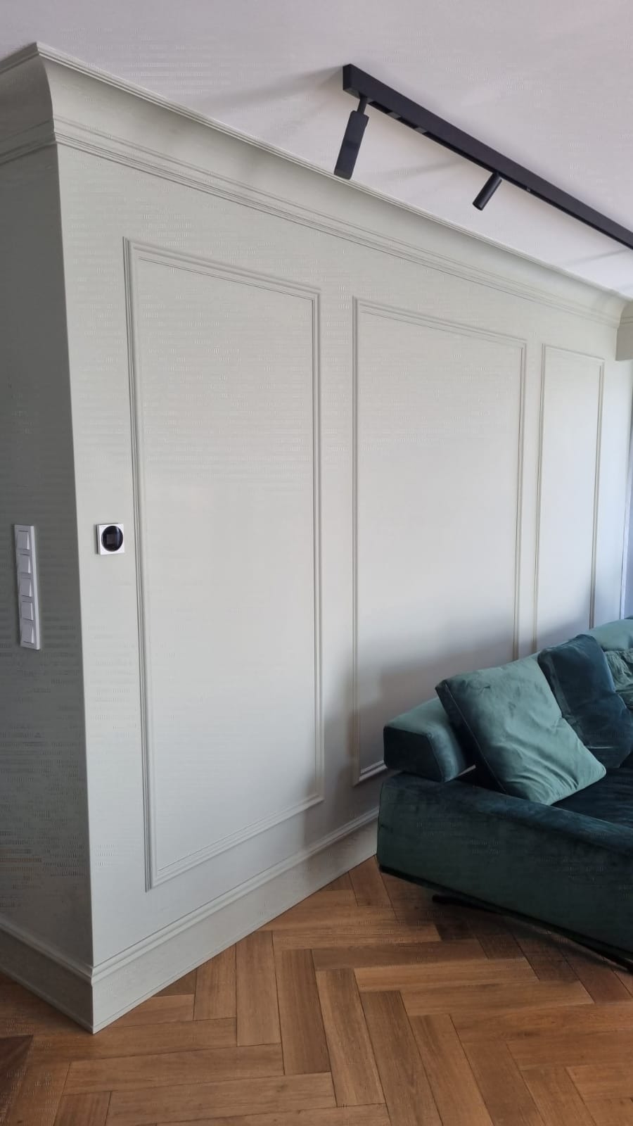 Eleganckie tapetowanie w stylu angielskim z delikatną teksturą, listwy dekoracyjne, parkiet w jodełkę i fragment zielonej sofy.