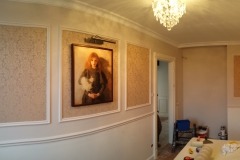 Eleganckie wnętrze z panelami ściennymi o wzorzystej strukturze, oświetlonym obrazem w ramie i ozdobnym żyrandolem.