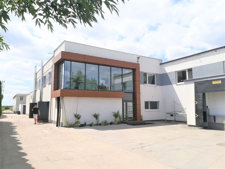 Nowoczesny budynek biurowy z przeszkloną fasadą i brązowymi elementami wykończeniowymi, widok z zewnątrz na dziedziniec.