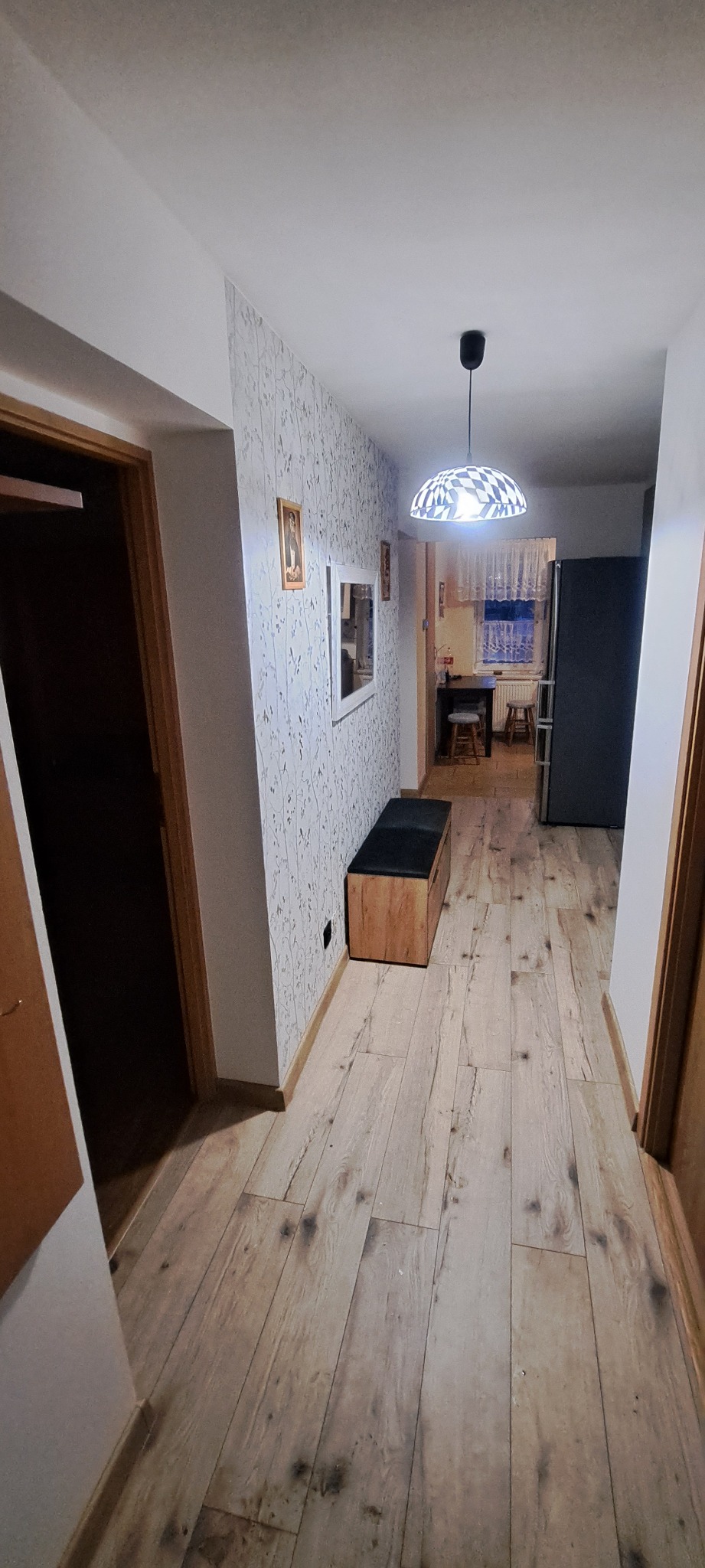 Korytarz po remoncie z panelami podłogowymi w odcieniach jasnego drewna, wzorzystą tapetą na ścianie i nowoczesną lampą sufitową w kształcie kuli.