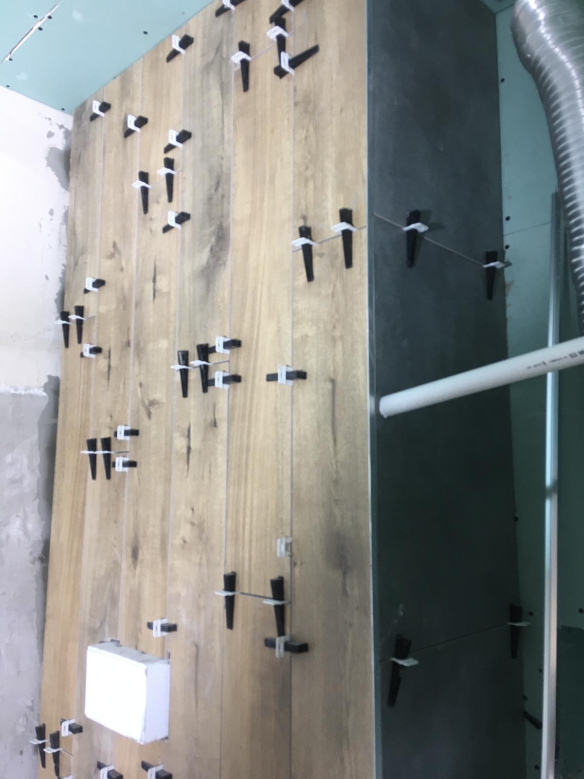 Układanie płytek imitujących drewno na ścianie, z użyciem krzyżyków dystansowych i sznurka do poziomowania, widoczny fragment instalacji wentylacyjnej.