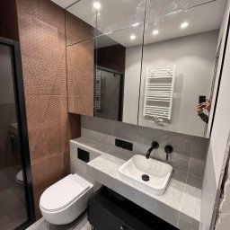 Daniel Glapa D.M.G. House Finish - Nowoczesna łazienka po remoncie: umywalka nablatowa, toaleta podwieszana, miedziane płytki strukturalne, lustro na ścianie, grzejnik drabinkowy.