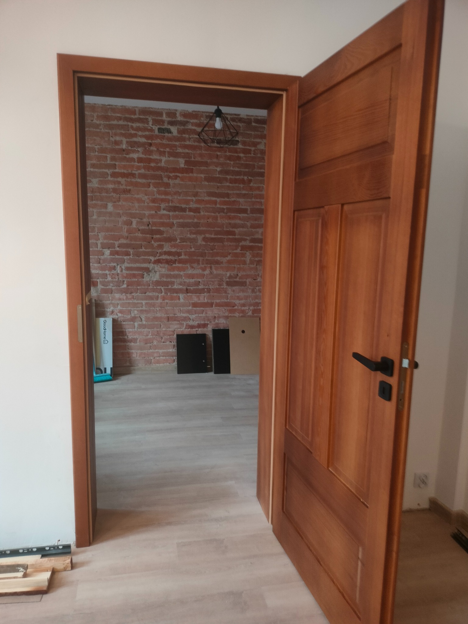 Otwarta, drewniana, fornirowana  ościeżnica w Pieńsku, z czarną klamką, widok na ceglaną ścianę i podłogę.