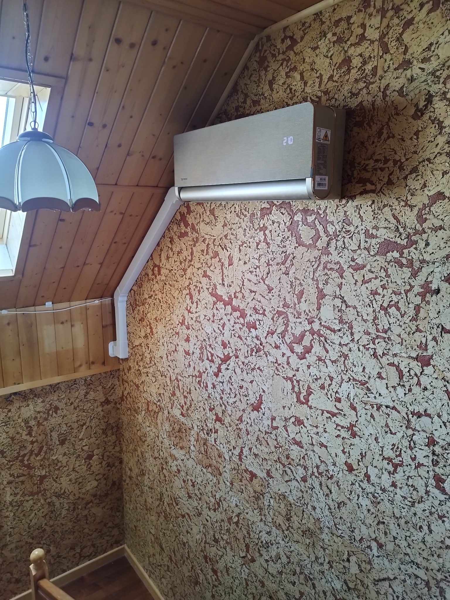 Klimatyzator ścienny z wyświetlaczem w drewnianym wnętrzu, Alwernia. Widoczna instalacja odprowadzająca skropliny. Dekoracyjna faktura ściany.