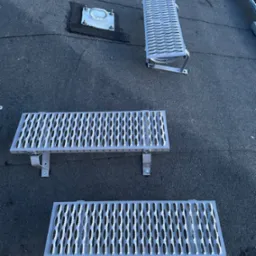 Metalowe podesty i drabina zamontowane na płaskim dachu pokrytym papą, zapewniające bezpieczny dostęp do urządzeń i kominów.