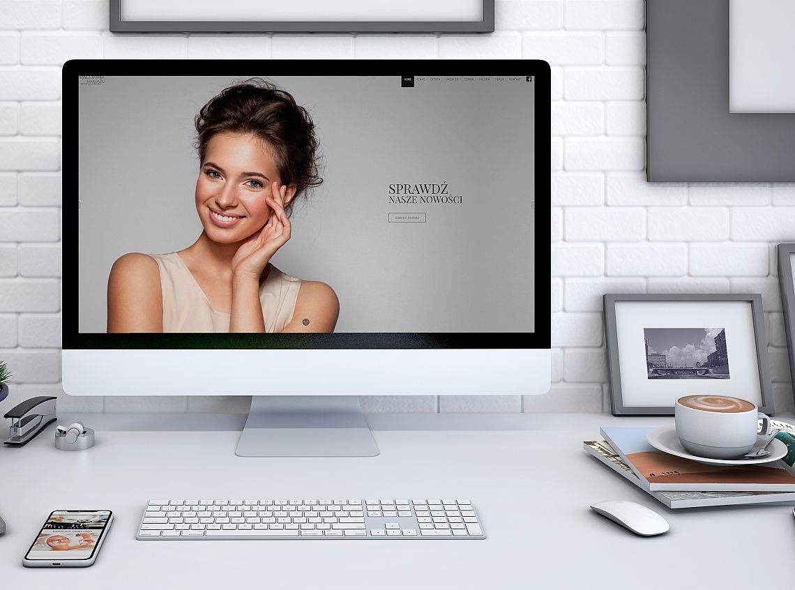 Monitor wyświetlający stronę internetową z uśmiechniętą kobietą, na biurku obok klawiatura, mysz, smartfon i filiżanka kawy