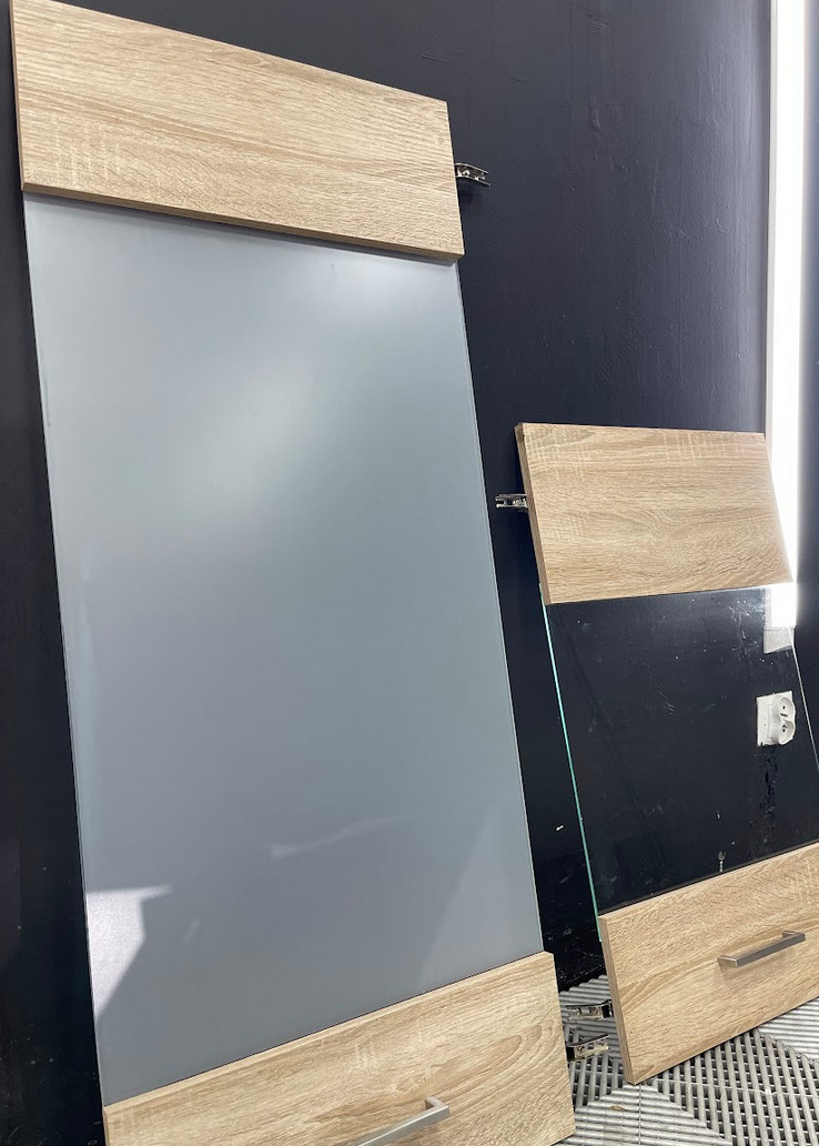 Dwie płyty meblowe z drewnopodobnym wykończeniem, jedna z szarą powierzchnią, druga z czarną, opierają się o ścianę w warsztacie.