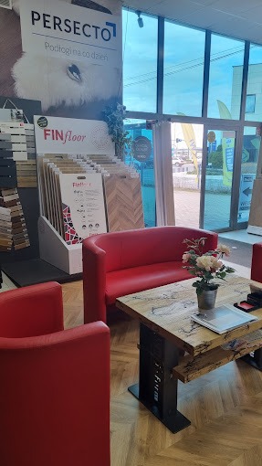 Wnętrze salonu z ekspozycją paneli podłogowych ułożonych w jodełkę, czerwone sofy i stolik kawowy z kwiatami w metalowej doniczce.