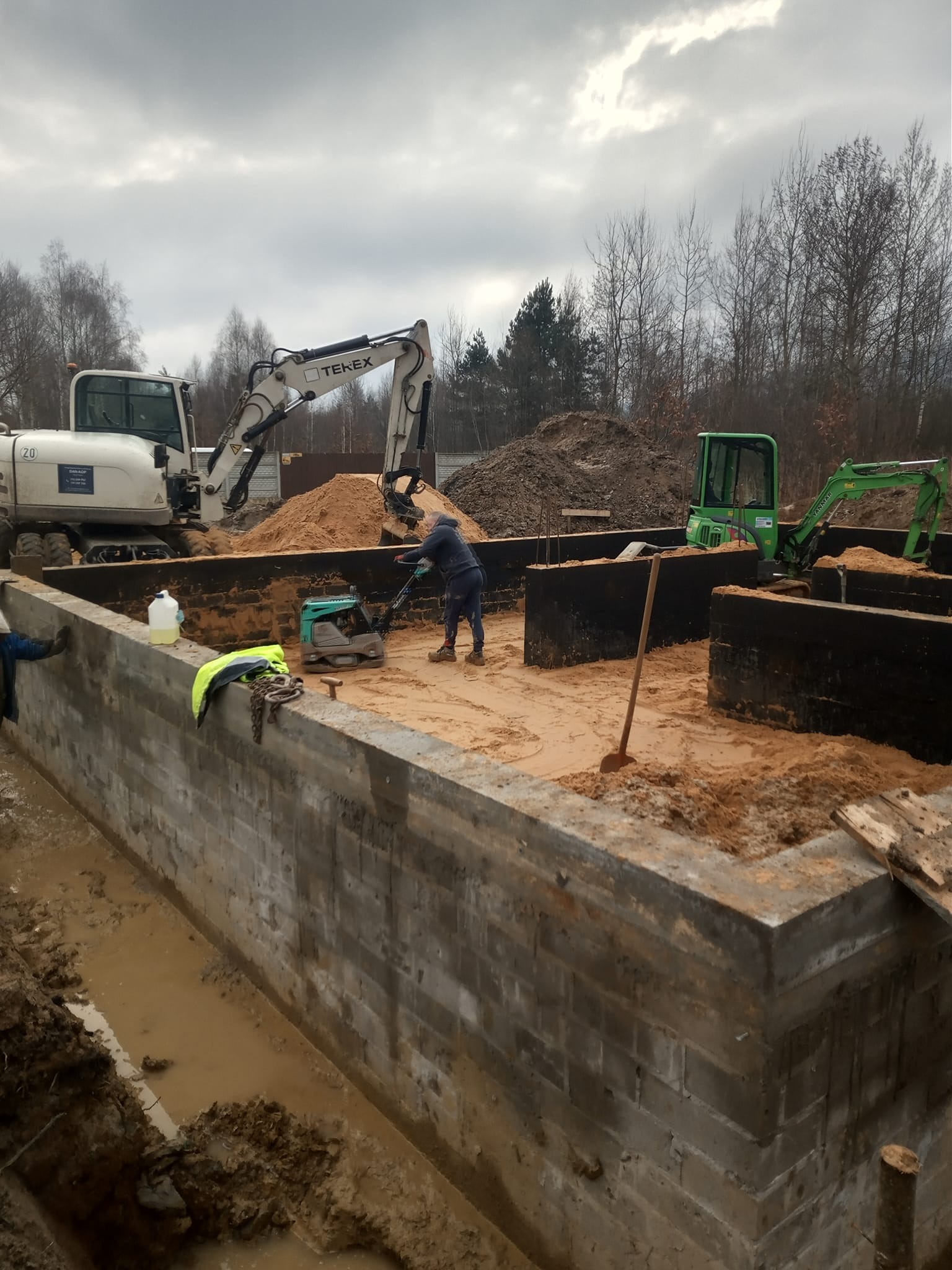 Fundamenty z bloczków betonowych, ubijarka, mini koparki na piasku, przygotowanie do wylewki, widok z góry.