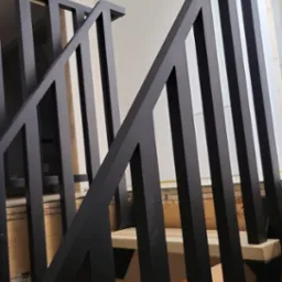 Nowoczesne schody z drewnianymi stopniami i minimalistyczną, czarną, metalową balustradą o pionowych szczeblach, widok z dołu, widoczne niedokończone wykończenie ściany.